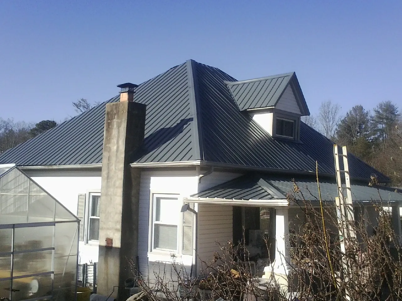 Dark blue standing seam metal roof on a white farmhouse with dormer — Slate & Tile Roof Repair by Roofing Brothers in North Greece