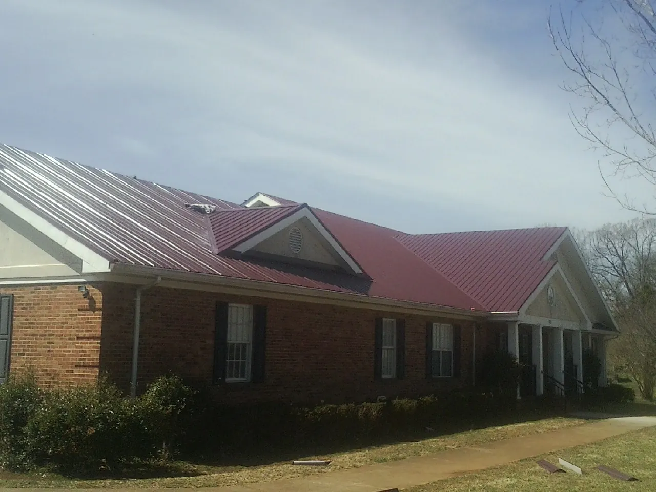 Red metal roof with gabled entries on a long brick building, from a Hail Damage Roof Repair job in North Greece