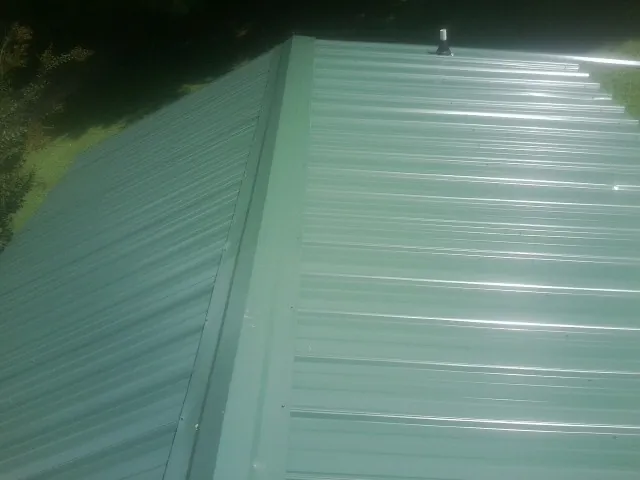 New green metal panels meeting at the ridge of a roof — Flat Roof Repair work by our crew in North Greece
