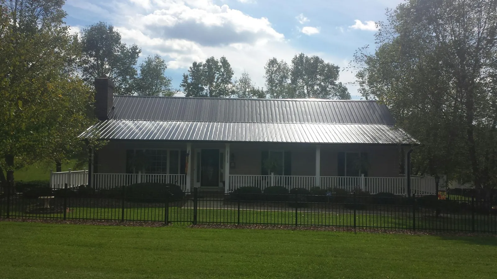 Gray metal roof on a brick ranch with a full width front porch — Gutter Guard Installation work by our crew in North Greece