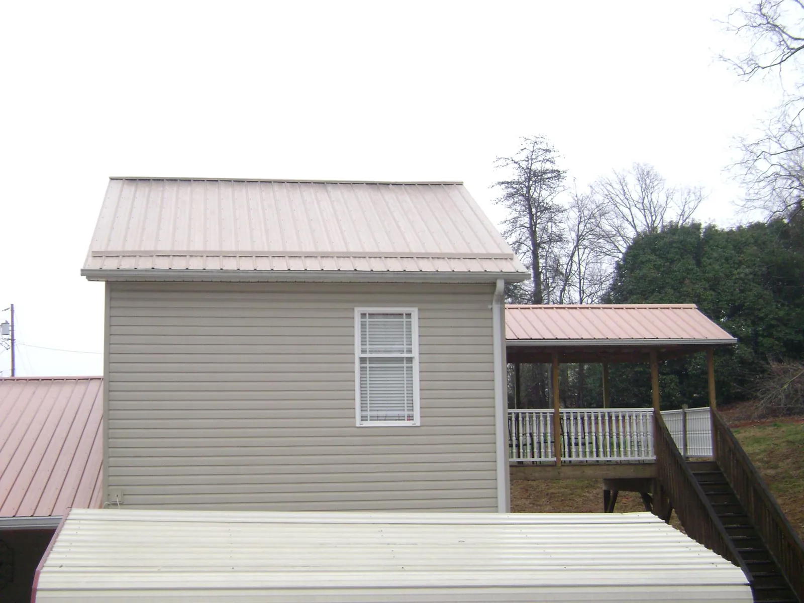 Tan metal roofs on a two story addition and attached porch, from a Roof Replacement job in North Greece